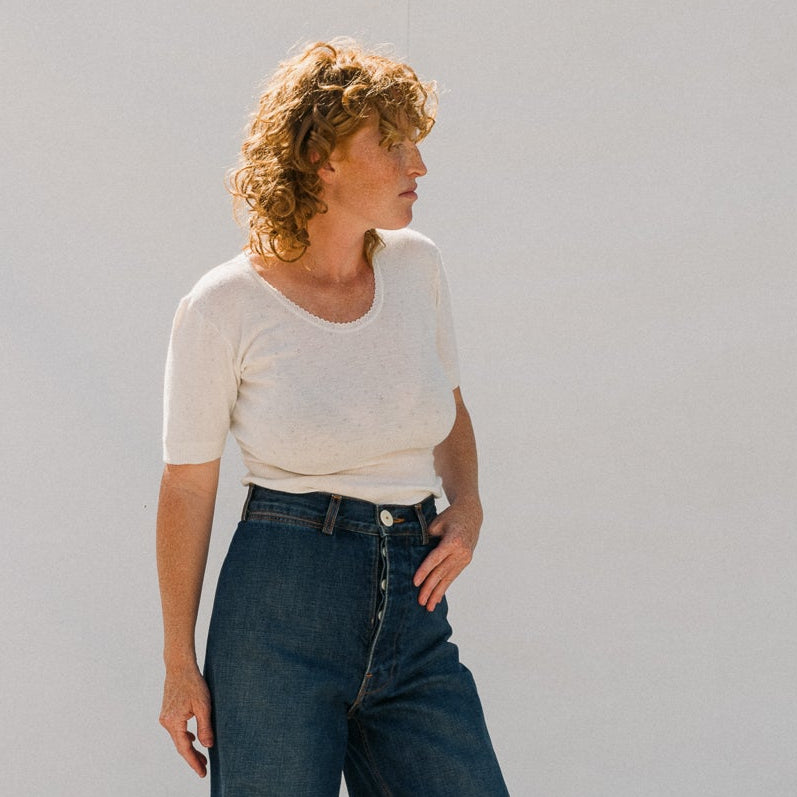 Woman wearing a white top and blue jeans standing against a light gray background