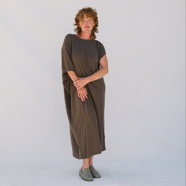 Person wearing a brown dress standing against a plain background