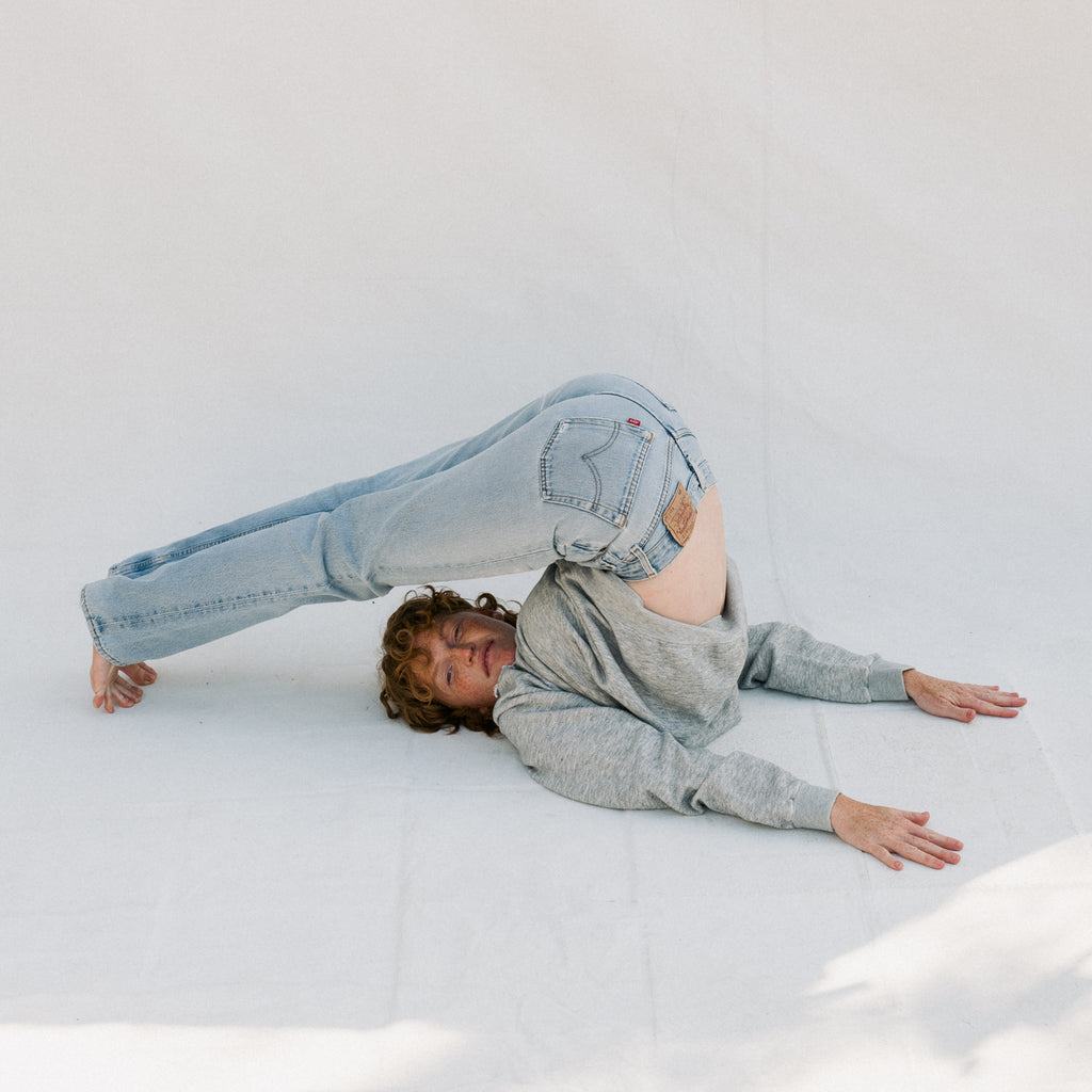 Person wearing light blue jeans and a gray sweater lying on a white surface.